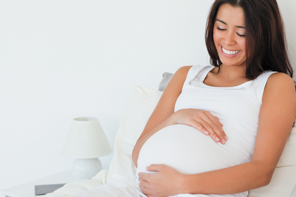 Healthy pregnant woman lying in bed holding belly