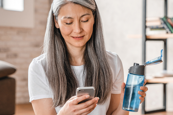 Person holding reusable water bottle and phone with digital workout