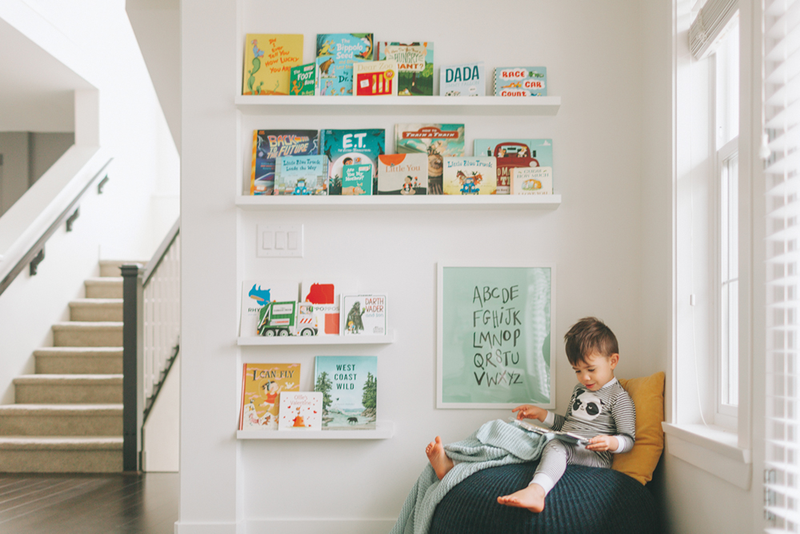 Kid sitting in corner of home reading surrounded by books on shelves