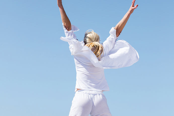 Back of person jumping in the air outside with arms spread open wearing all white