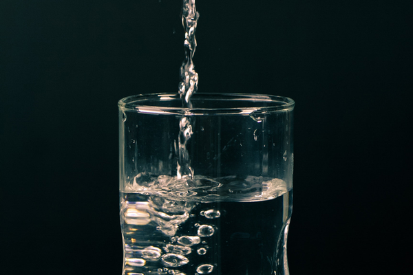 Glass with clean drinking water being poured in against black background