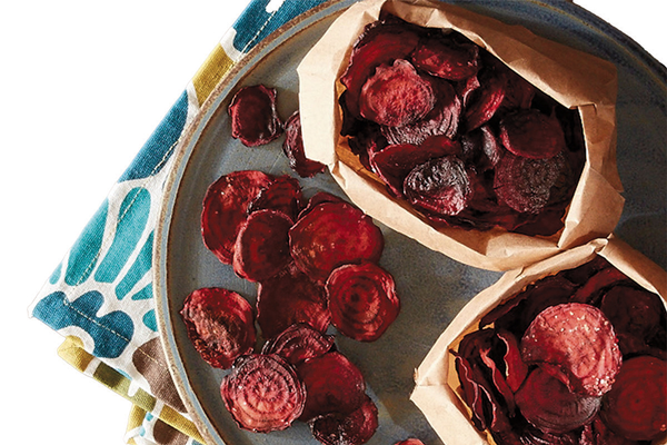 Tray of beet chips inside paper bags on floral cloth