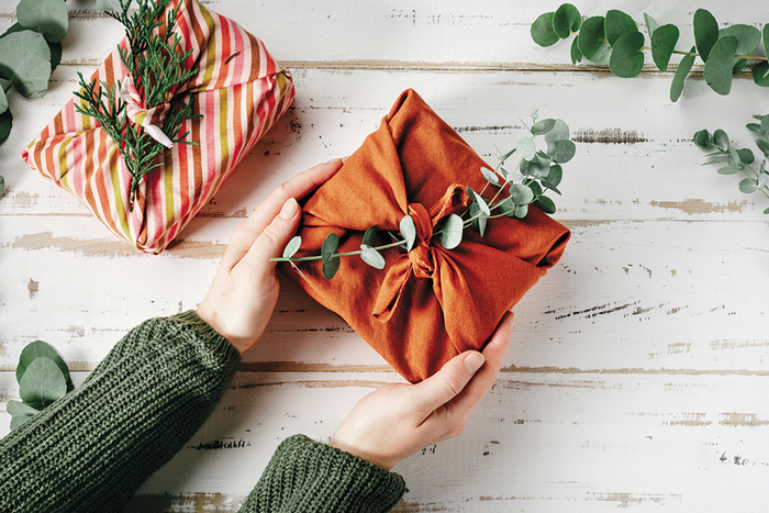 Hands outstretched holding gift wrapped in cloth fabric and eucalyptus sprig