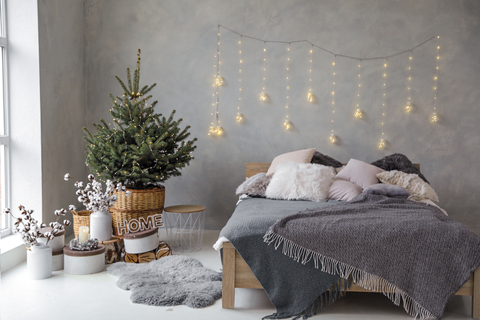 Bedroom decorated with holiday decor including string lights behind bed and live potted Christmas tree