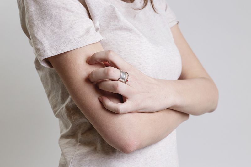 Person scratching psoriasis on upper arm